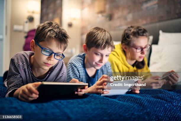 kids playing with modern mobile devices - three people in bed stock pictures, royalty-free photos & images