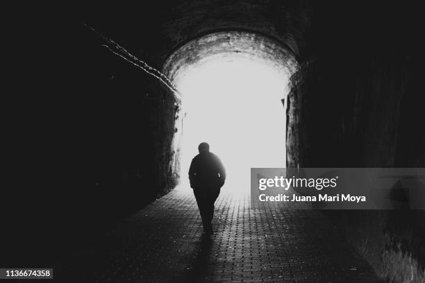 rear view silhouette of a senior man walking towards the light at the end of the tunnel - approaching imagens e fotografias de stock