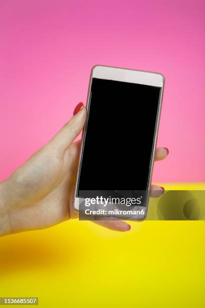 cropped hand of woman holding mobile phone over colored background - drogados imagens e fotografias de stock