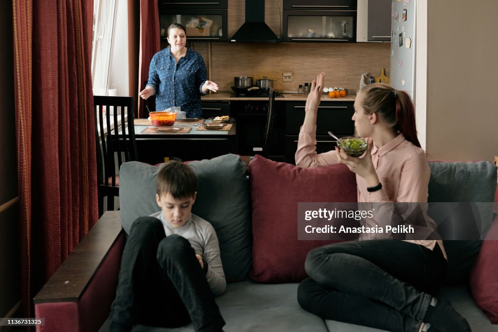 Strict middle-aged plus-size mother in casual shirt fighting with adult daughter who refusing to eat at table in kitchen, mother calling children in to dinner