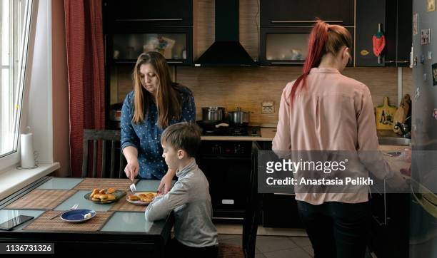 serious attractive natural woman in plus-size shirt standing at table and putting nuggets into sons plate while serving table for family dinner at home - eating nuggets ストックフォトと画像