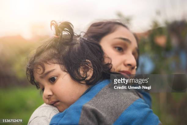 trieste moeder knuffelen haar kleine dochter buitenshuis - indian mother stockfoto's en -beelden