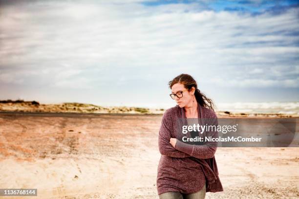 mujer joven brroding caminando en la playa solo abrazándose a sí mismo - in case of discomfort fotografías e imágenes de stock