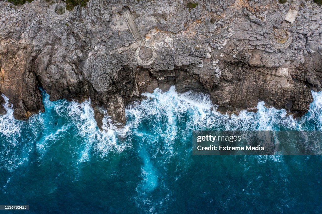 A view directly above a steep rocky shoreline coming out of the sea