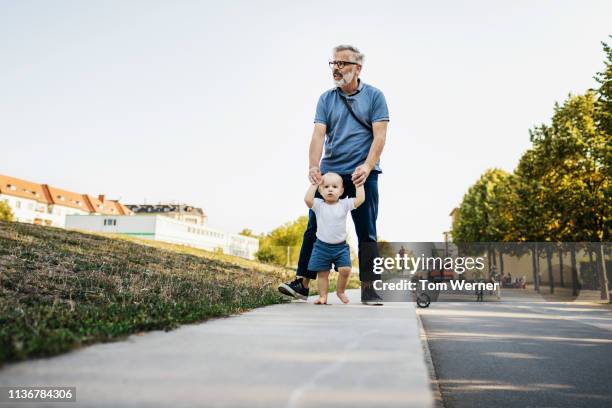 grandpa holding grandson's hands while they walk - weggucken stock-fotos und bilder