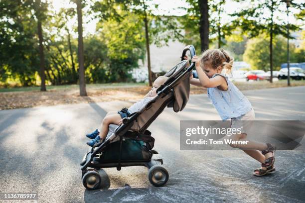young girl pushing baby brother in stroller - brother toddler sister stockfoto's en -beelden