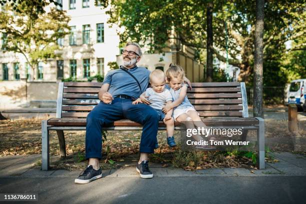 grandpa sitting on bench with grandchildren - menschen sitzend stock-fotos und bilder