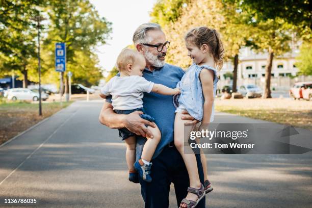 grandpa holding two grandchildren at the park - baby beard stock-fotos und bilder