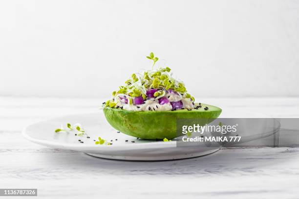 avocado garden stuffed with tuna, mayonnaise, red onion, black sesame seeds and radish sprouts - prato de comida imagens e fotografias de stock