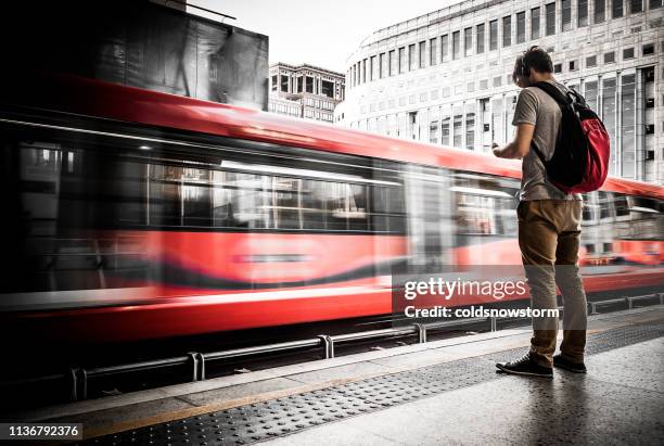 young man waiting at train station with speeding train motion blur - london train stock pictures, royalty-free photos & images