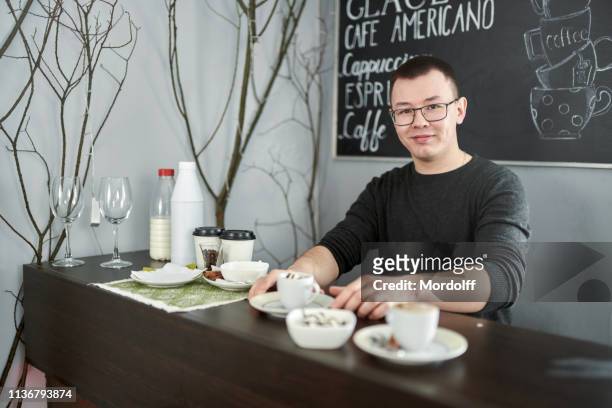 young man barista bietet kaffee im cafe counter - irish coffee stock-fotos und bilder