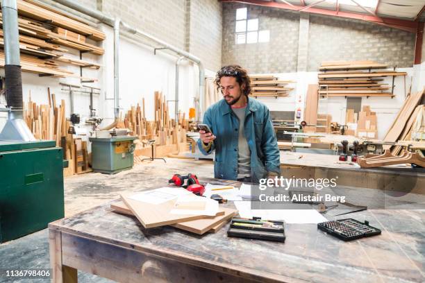 designer looking at smartphone while working in a furniture factory - entrepreneur manufacturing stockfoto's en -beelden