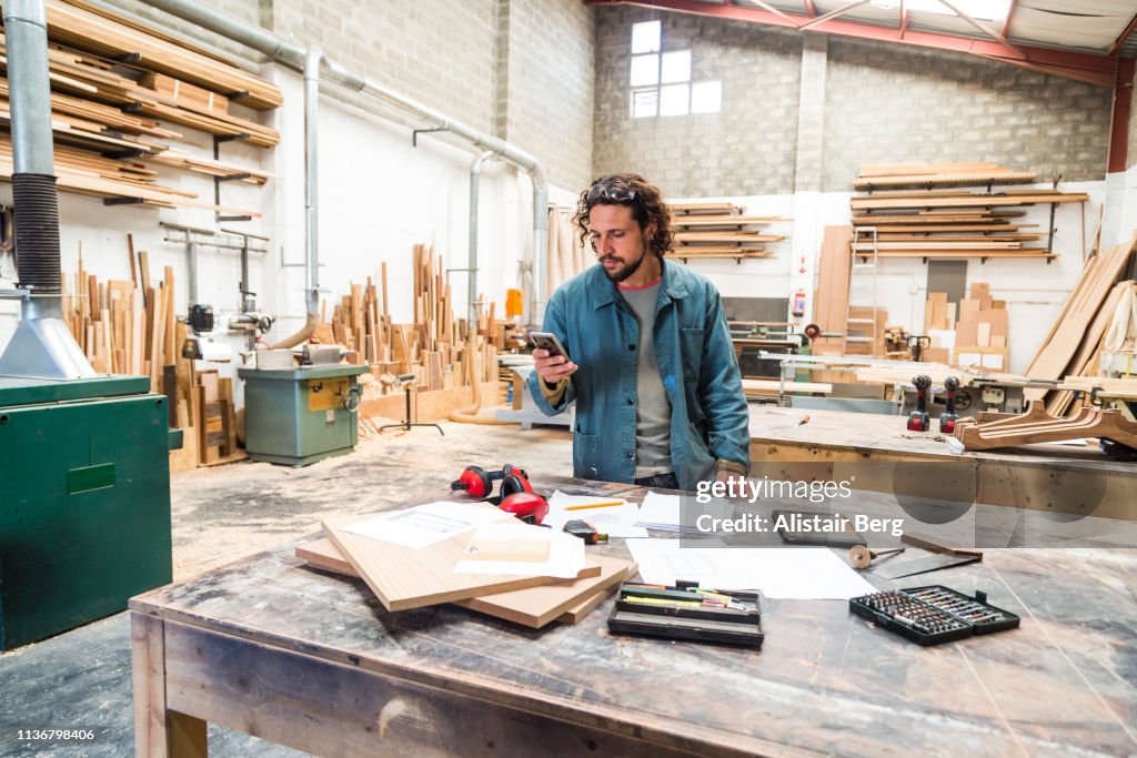 Designer looking at smartphone while working in a furniture factory