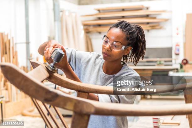 Female black worker restoring an old chair in a woodworking studio