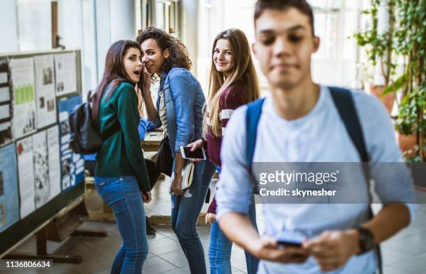 ragazze adolescenti sorridenti che spettegolano sul loro amico maschio in un corridoio della scuola. - rumor foto e immagini stock