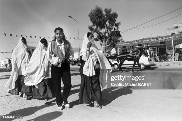 Jeune femme habillée à la mode occidentale accompagnée de femmes en tenue traditionnelle, dans la rue à Douz, en novembre 1996, Tunisie.