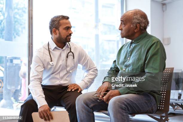 serious man is staring at doctor in waiting room - three quarter length stock pictures, royalty-free photos & images