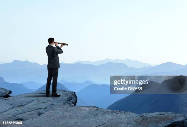 geschäftsmann mit spyglass looking out in richtung mountain range - business aspiration looking stock-fotos und bilder