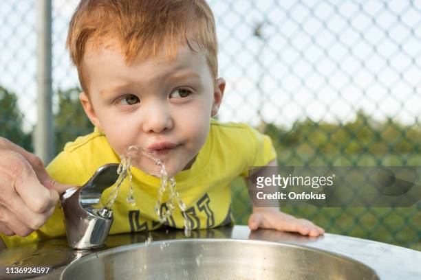 lindo pelirrojo niño bebiendo agua de fuente de agua - fountain fotografías e imágenes de stock