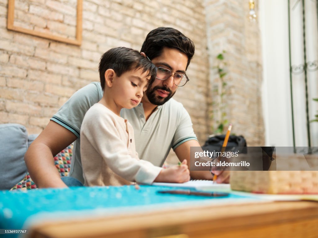 Mexican father and young son drawing on notebook at home