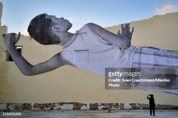An image by French artist JR called "Giants" is displayed of a boy looking over a wall during the 13th Havana Biennial on April 13, 2019 in Havana,...