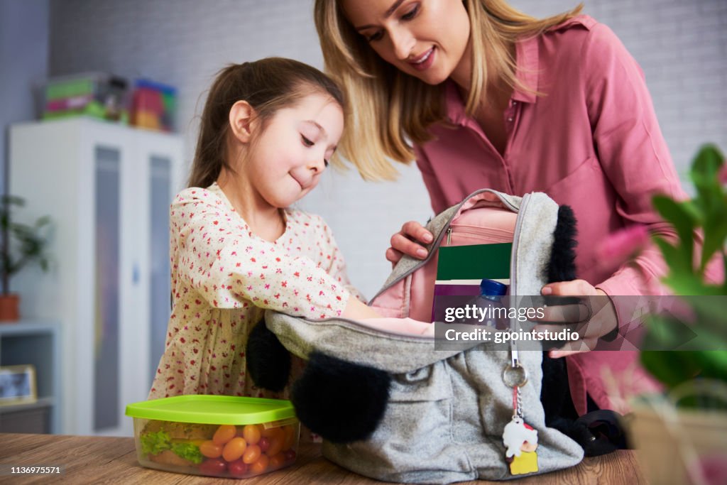 Young mum and daughter packing backpack for the school