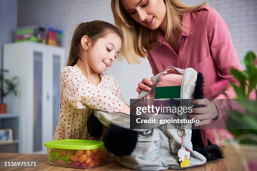 Young mum and daughter packing backpack for the school Young mum and daughter packing backpack for the school