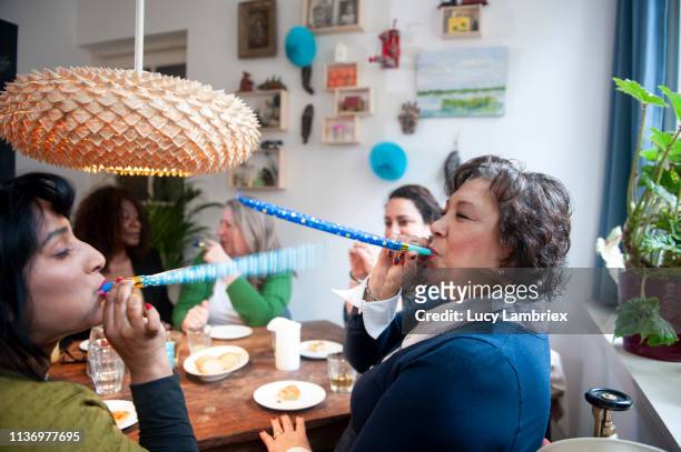 mixed group of women celebrating friend's birthday with a party, playing with party horns - absurd birthday stock pictures, royalty-free photos & images