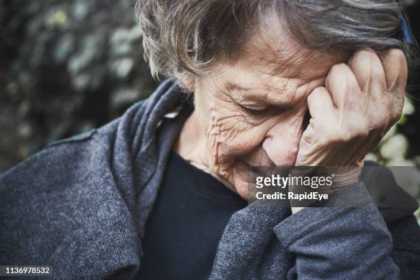 senior vrouw, hoofd in handen, ziet er wanhopig moe en ongelukkig - hopelessness stockfoto's en -beelden