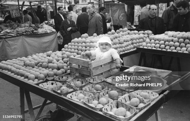 Bébé dans une cagette de fruits sur le marché d'Aligre à Paris, dans les années 1970, France.