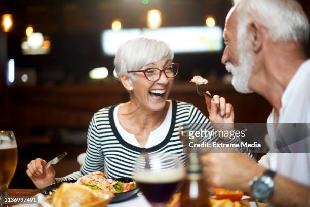 お互いに餌を与え、レストランで食事中に楽しい時間を持つシニアカップル - dining restaurant ストックフォトと画像