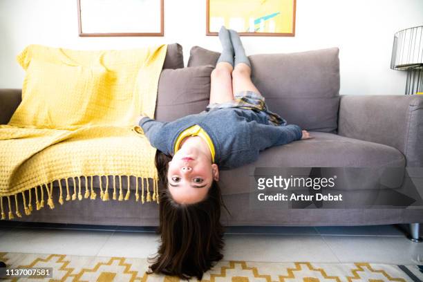 funny girl upside down in the sofa playing looking at camera. - girl upside down stock pictures, royalty-free photos & images