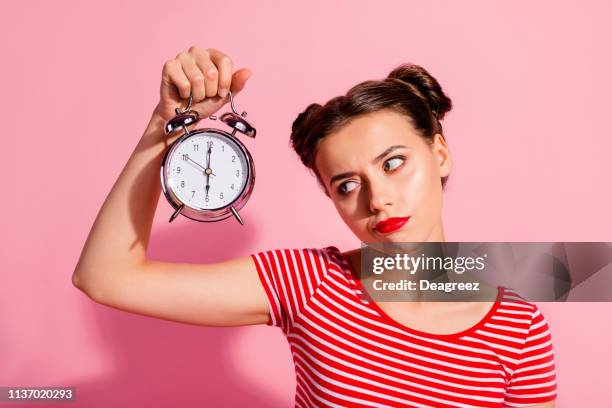 Close-up portrait of her she nice cute charming attractive glamorous sad teen girl wearing striped t-shirt holding in hand showing clock boring hour isolated over pink pastel background