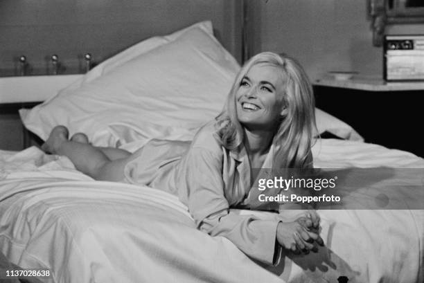English actress Shirley Eaton pictured in character as Jill Masterson, lying on a bed wearing a pale blue shirt on the set of the James Bond film...