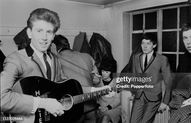 English musician Graham Nash, singer and guitarist with The Hollies, pictured with an acoustic guitar in a dressing room backstage during a tour by...