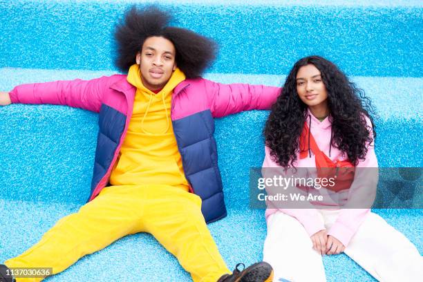 fashionable couple sitting on blue floor - vestito multicolore foto e immagini stock