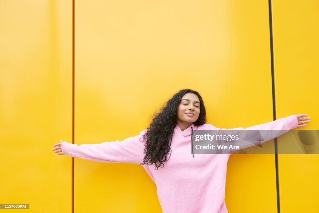 Woman with arms outstretched against yellow background