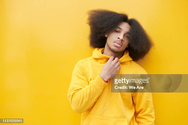 man wearing a yellow sweatshirt standing against a yellow background - afro frisur stock-fotos und bilder