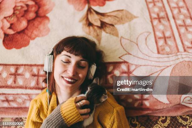 relaxed girl with cat enjoying good music at home - girls cuddling cat stock pictures, royalty-free photos & images