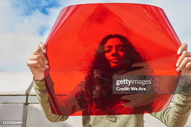 young woman holding up red filter in front of face - regla fotografías e imágenes de stock