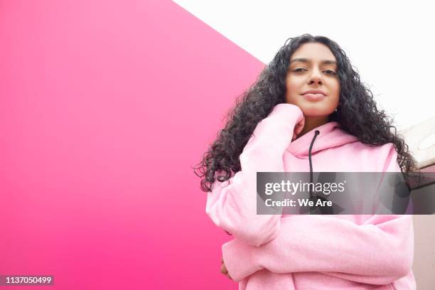 woman in pink hooded sweatshirt near pink wall - main au menton photos et images de collection