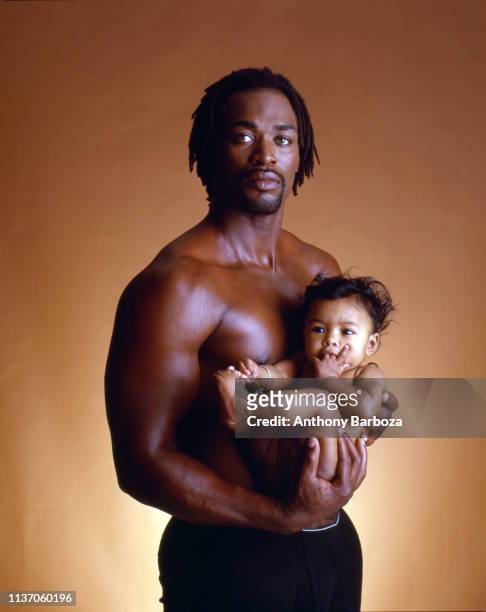 Portrait of a shirtless man as he holds in an infant in his arms, New York, 1990s.