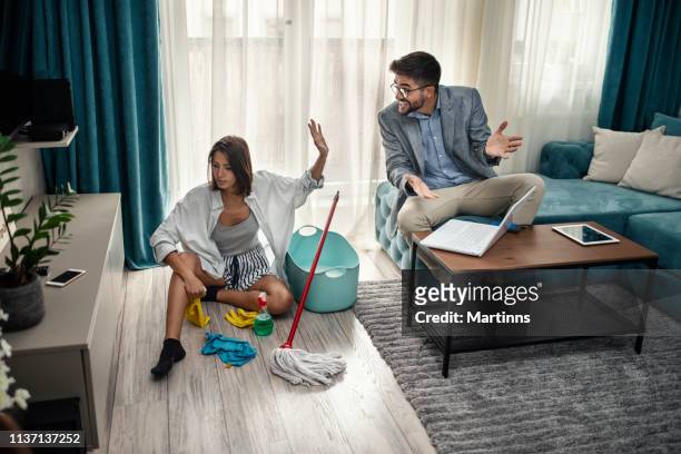 woman cleans the floor at home while her lazy man sits on the couch and uses a laptop - inequality stock pictures, royalty-free photos & images