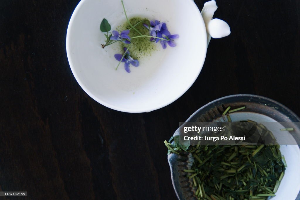 Ceramic tea brewing vessel with wet leaves and stems of Kukicha and white cup in fine bone China.