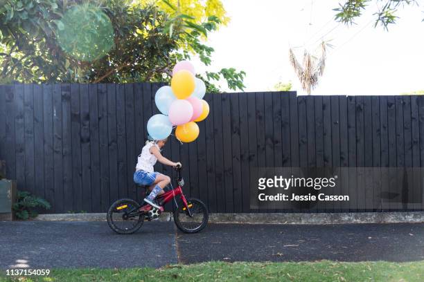 a girl rides her bike with colourful balloons - cycling streets stock pictures, royalty-free photos & images