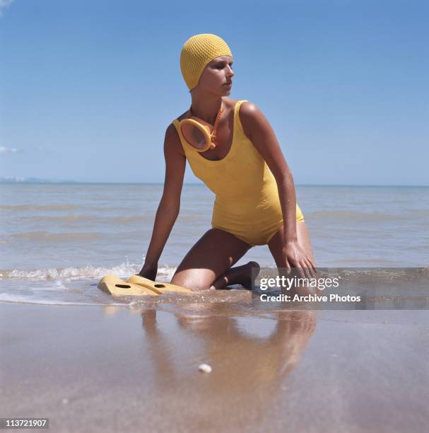 Model wearing a yellow swimsuit with matching accessories on the beach, circa 1975.