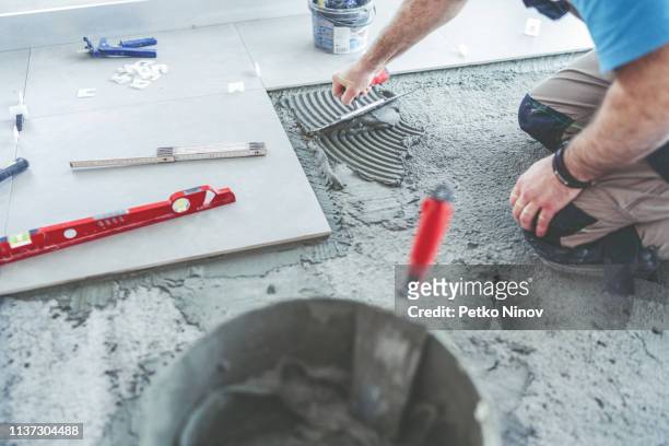 professional tile mason spreading adhesive on the floor - azulejo imagens e fotografias de stock