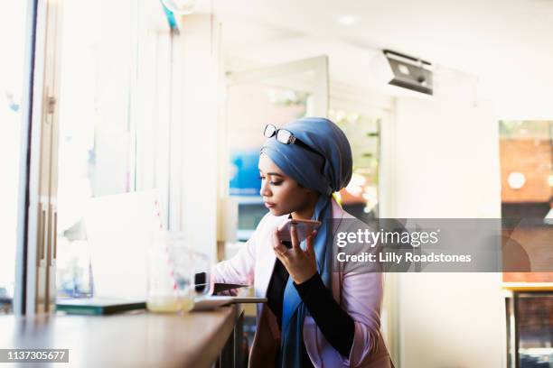 young muslim woman working in cafe - woman entrepreneur looking at phone stock-fotos und bilder