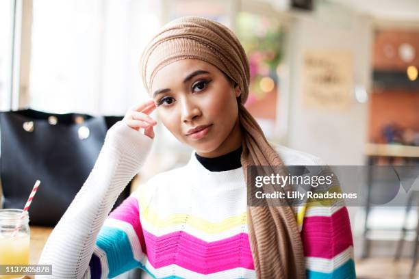 one young muslim woman sitting in cafe looking at camera - hijab fashion stockfoto's en -beelden