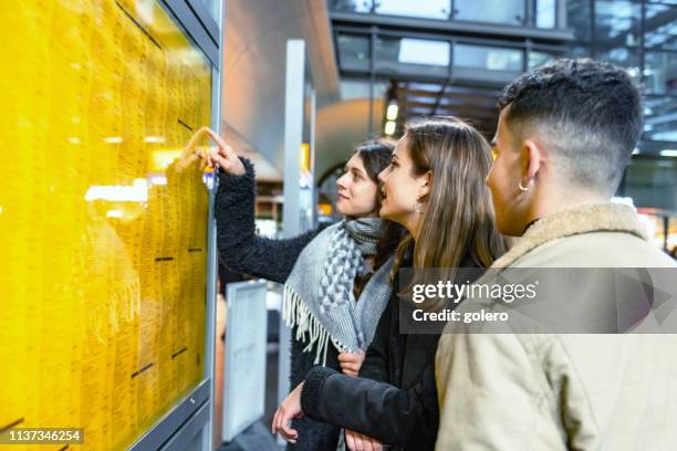 three young travellers checking train connection on time-table - train arrival stock pictures, royalty-free photos & images